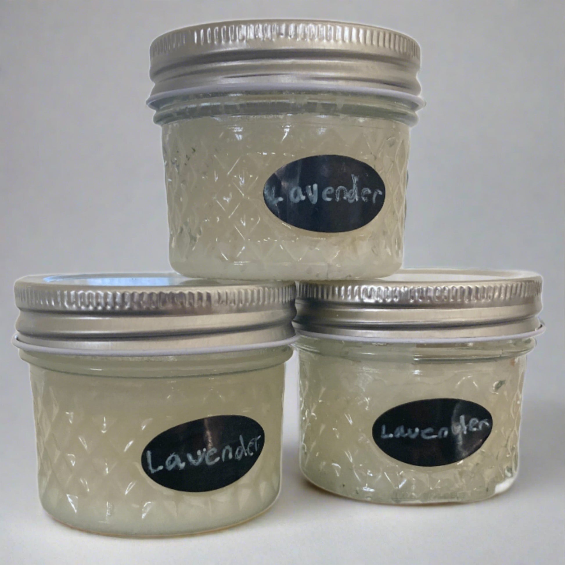 This photo is of three jars of sugar hand scrub stacked with two on the bottom and one on top. The scrub is scented in lavender and made with organic coconut oil, sugar, and essential oil.